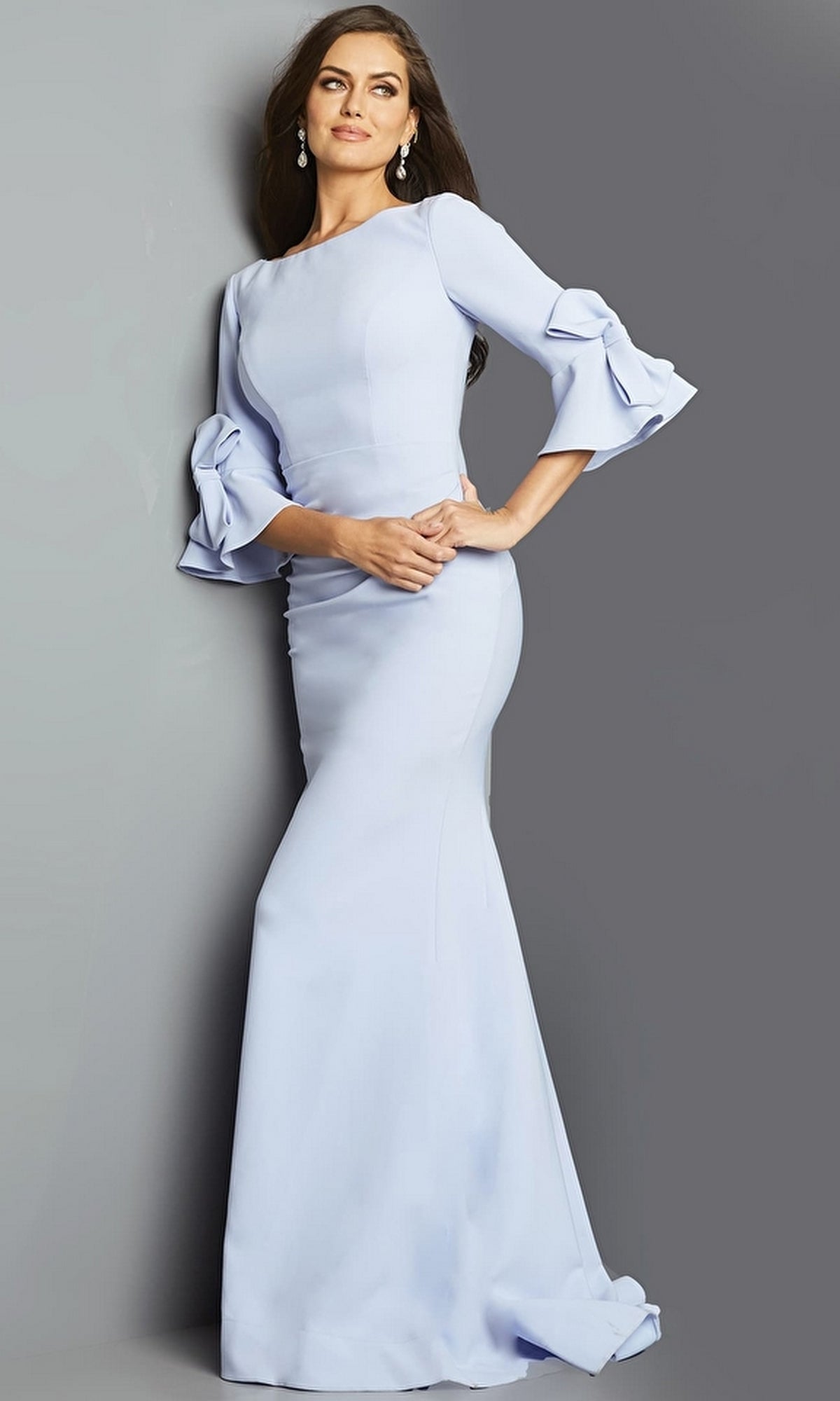 A woman in the Long Formal Jovani Dress 09776, a light blue evening gown with ruffled bell sleeves, stands against a gray background.
